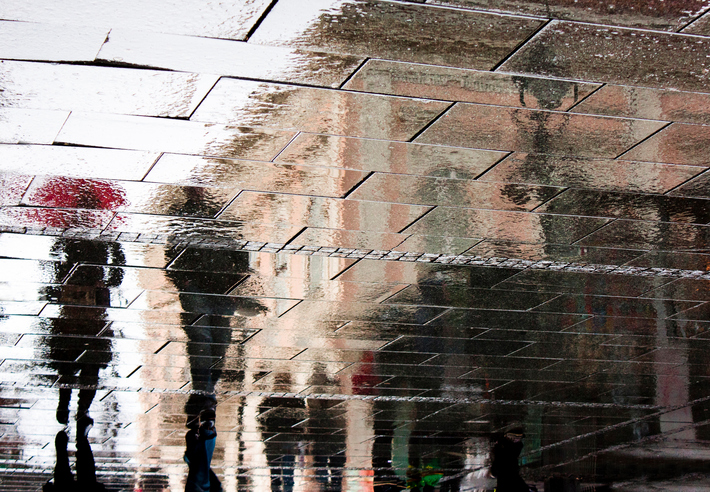 Reflection of people walking on sidewalk covered in rain