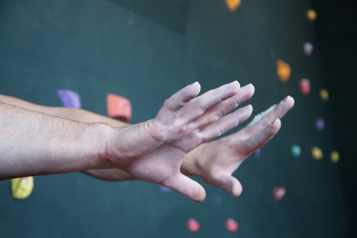Chalk-covered hands outstretched in front of rock climbing wall