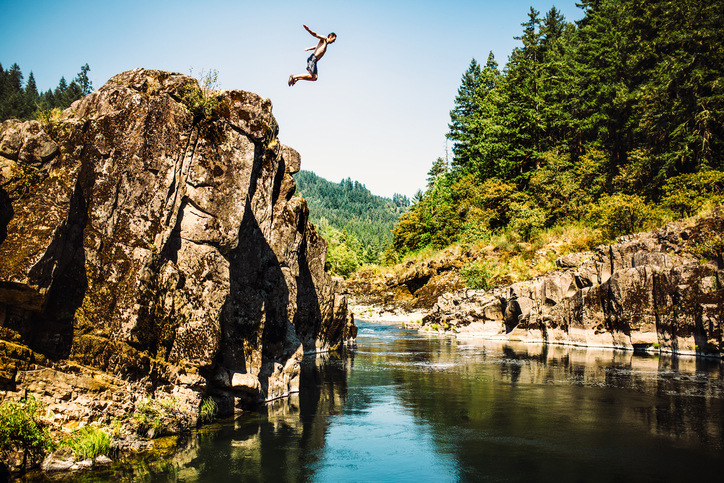Man jumping off of rock ledge into water