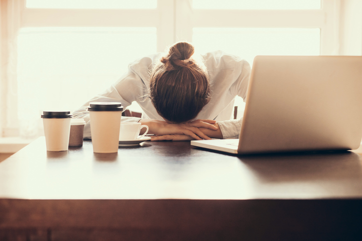 Woman surrounded by cups of coffee with her head on her desk