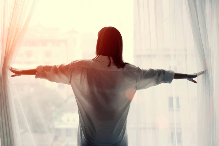 Woman opening curtains and looking out window