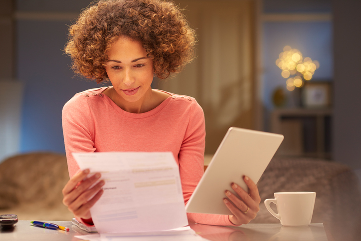 Woman at table, comparing paperwork and tablet