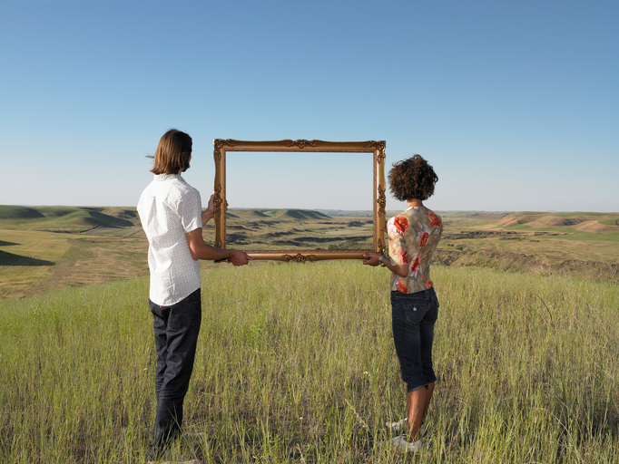 A man and woman hold a picture frame to the distant horizon.