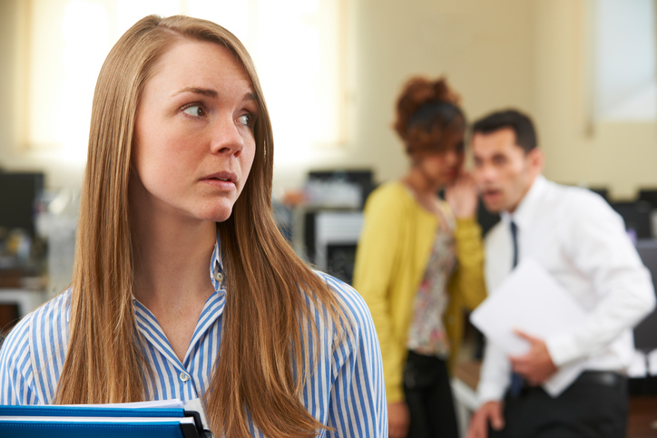 A woman looks worried as she sees coworkers laughing behind her.