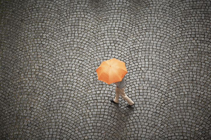 Person covering their head with an orange umbrella and walking on swirled, grey cobblestone