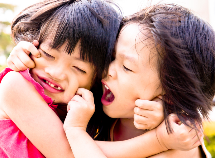 Two young sisters pinch each other's faces.