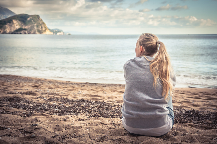 Woman in grey sweatshirt sitting at beach on cloudy day