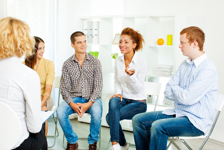 Support group meeting in modern setting, people are talking and gesturing