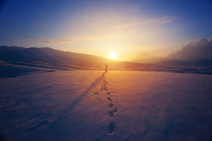 Tracks in snow leading up to person during sunset