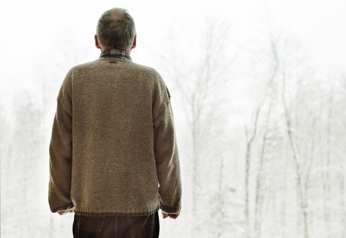 A balding man watches snow fall on trees.