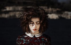 Artistic photo of person with chin-length curly hair looking down against clouded background