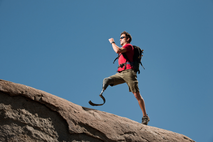 A man with a red shirt and a prosthetic leg climbs a mountain.
