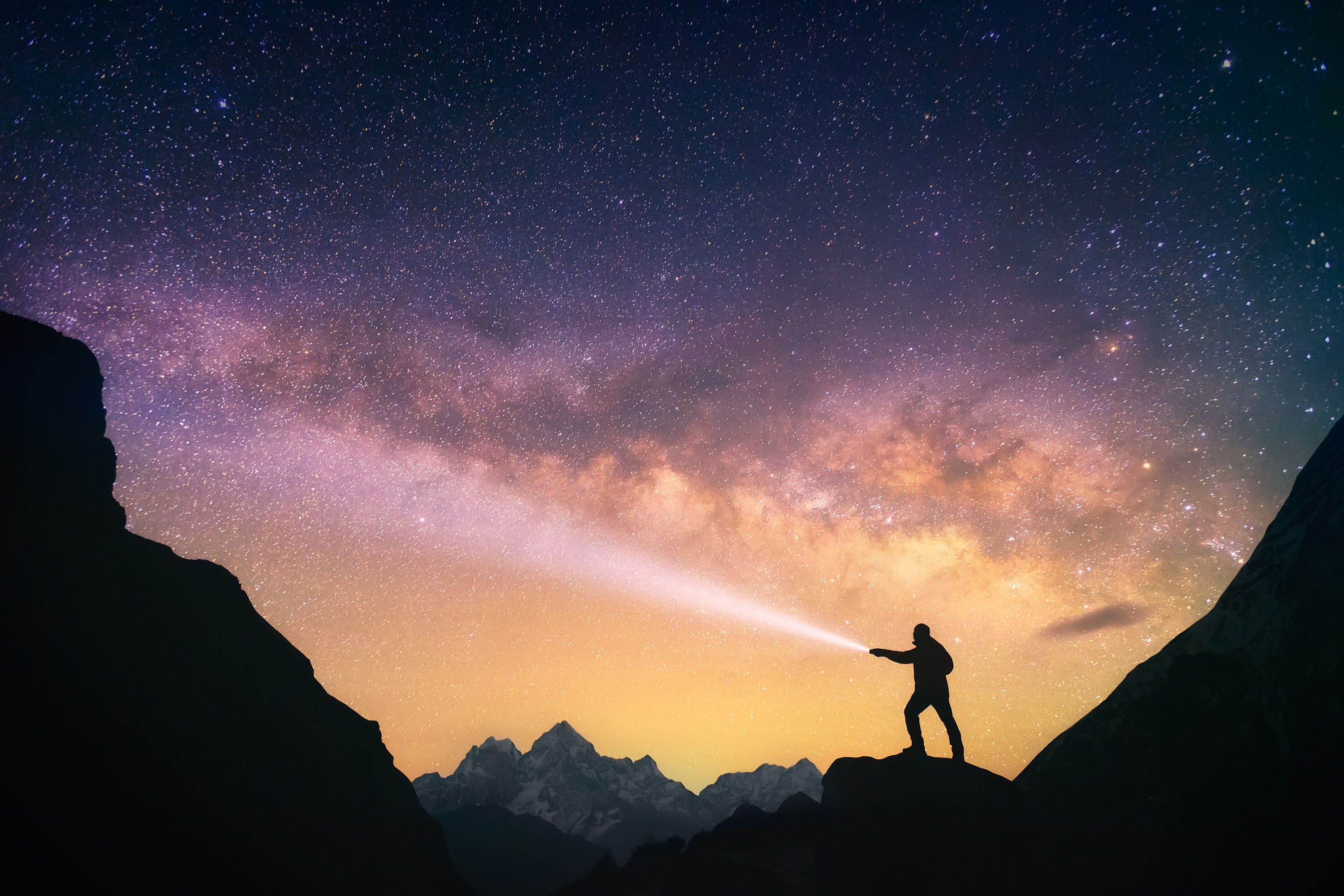 Man shining flashlight at starry sky in mountains