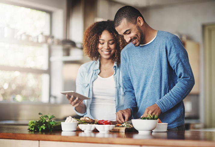 A young couple smiles as they cook together.