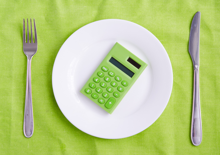 A green calculator sits on a white plate. The tablecloth is also green.