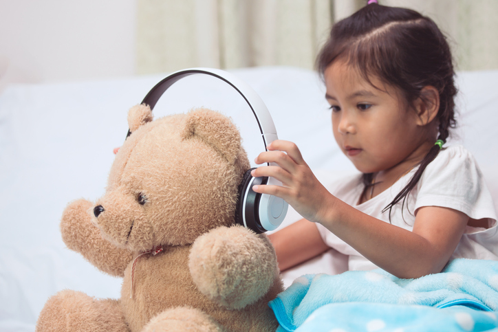 A young girl puts headphones on her teddy bear.