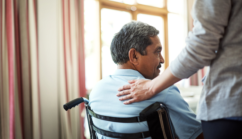 A senior man in a wheelchair glances backward when someone touches his back.