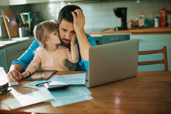 A man frets over bills while his young daughter sits in his lap.