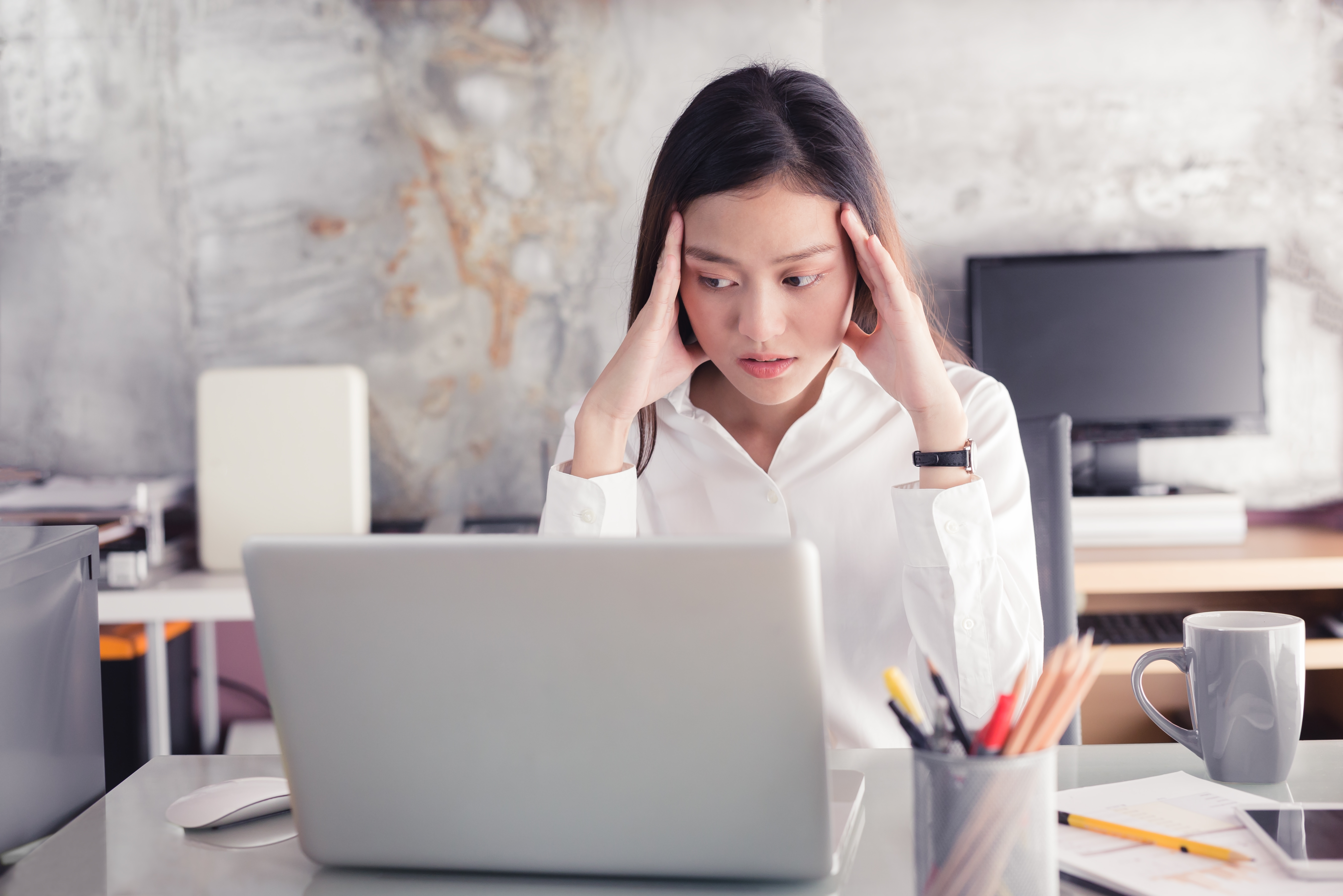 Woman sitting at desk with head in hands, stressed