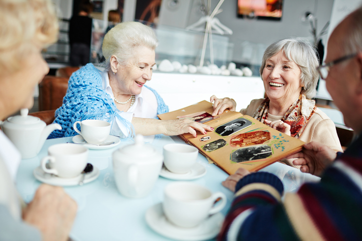 A group of seniors look over a photo album while drinking tea.