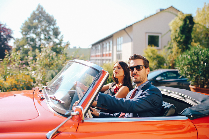 A man pulls up in a red sports car. A beautiful woman sits in the seat next to him.