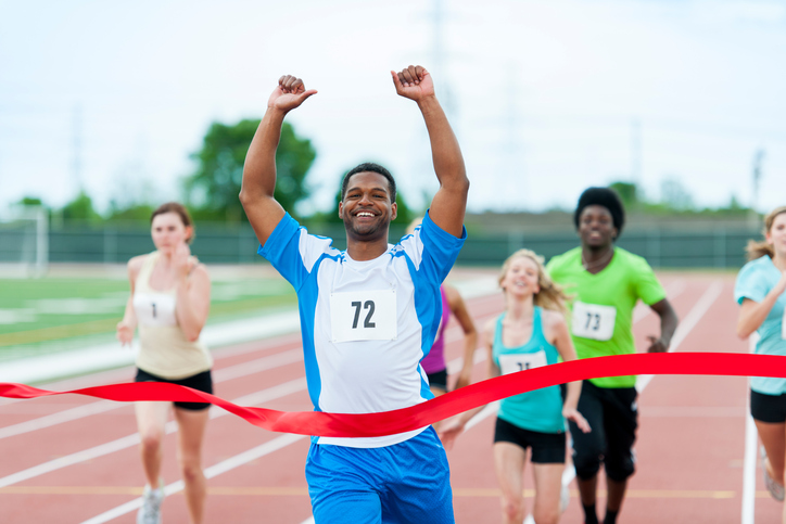 A man sprints across the finish line of a race, holding his hands up in victory.