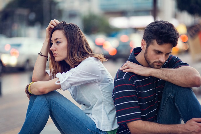 Sad couple sitting back-to-back outside