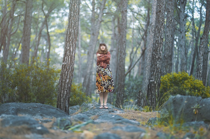 Woman stands alone in the middle of a forest.