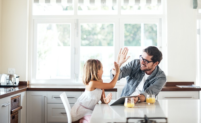 Father high-fives daughter while the two play a game together at the breakfast table.