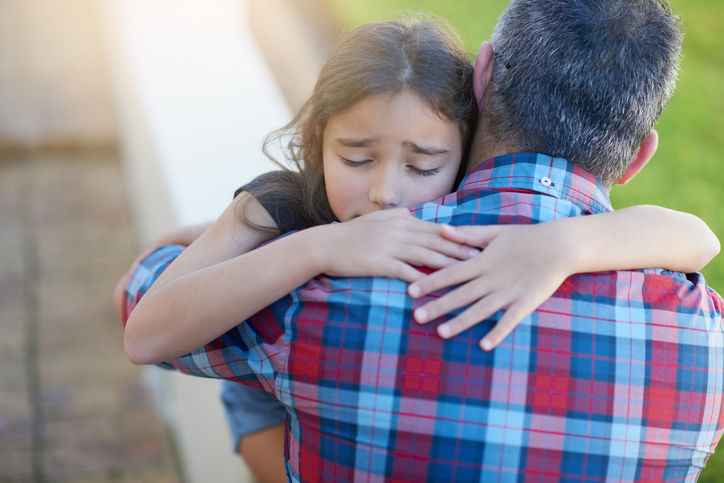 A sad girl hugs her father.