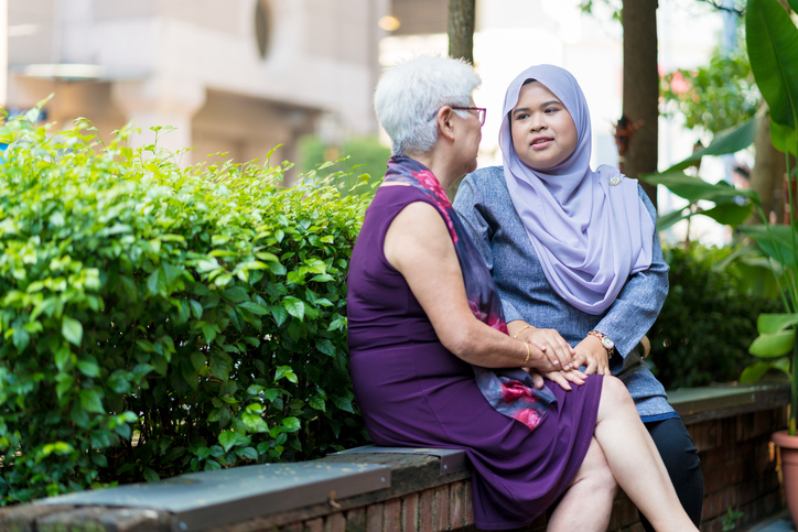 A woman comforts her elderly mother on a bench.