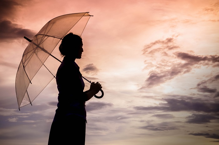 Silhouette of woman standing under umbrella, facing a darkening sky.
