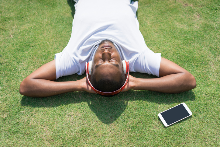 A man relaxes on some grass while listening to an app for breathing exercises.