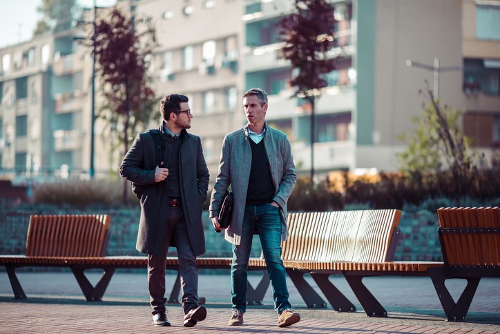 Two men chat as they walk along an empty street.