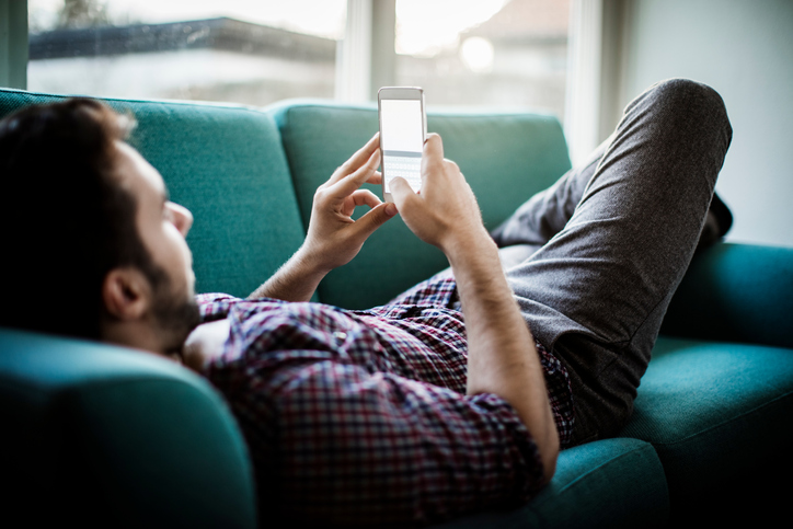 Young man alone on couch checking social media.