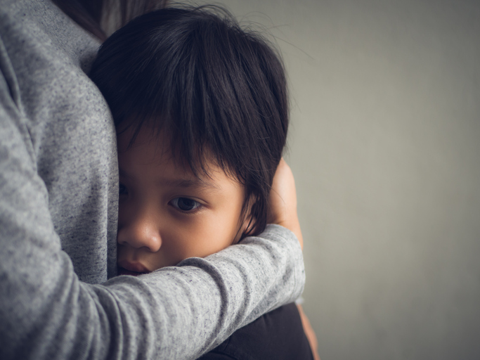 A toddler stares into space while his mother hugs him.