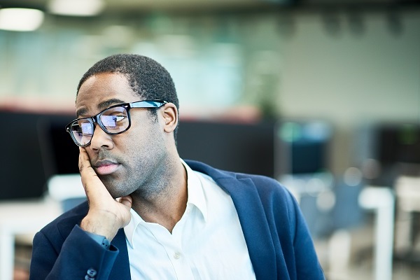 Man sits at desk with head in hands, looking worried.