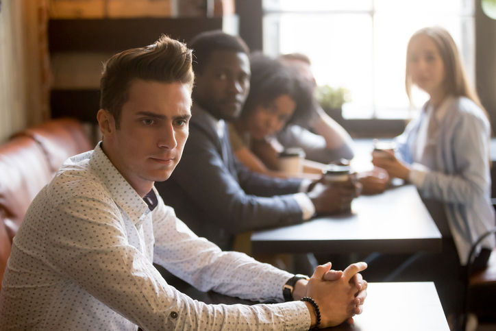 A man sulks while his worried friends stare at him.