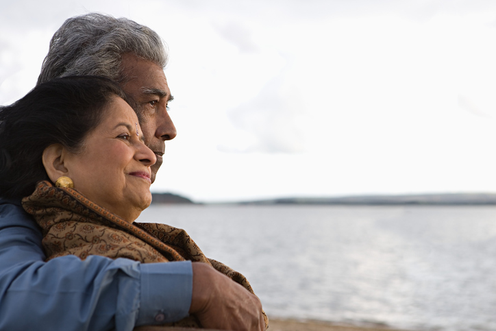 A man puts an arm around his wife as they look at the gray sea.