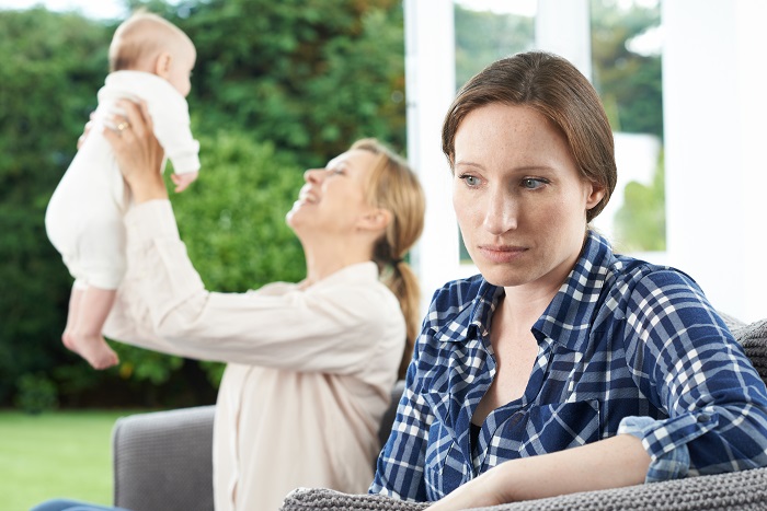Woman looks unhappy while her friend holds her baby.