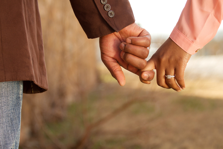 Close-up of engaged couple locking fingers.