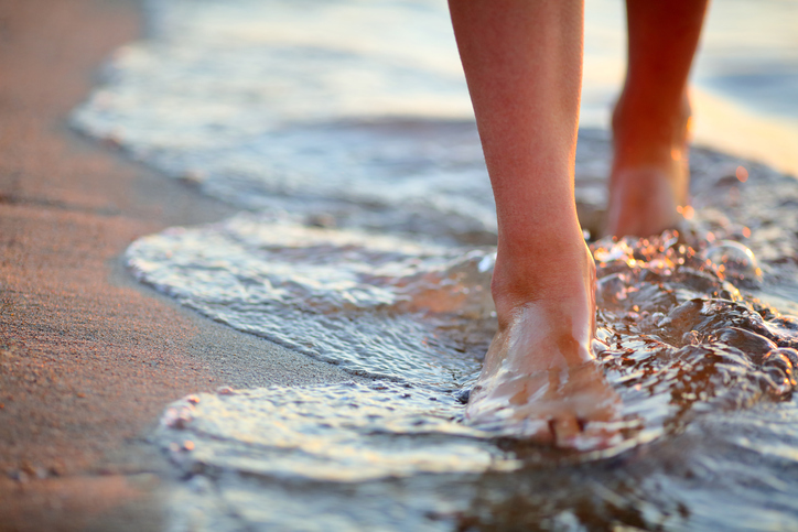 Close-up of woman's feet walking through ocean waves toward the camera.
