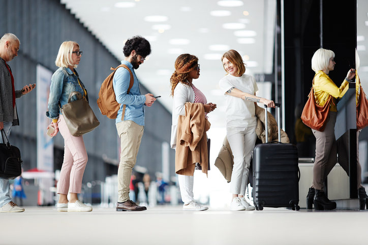 People of varying ethnicities and ages wait in line at the airport.