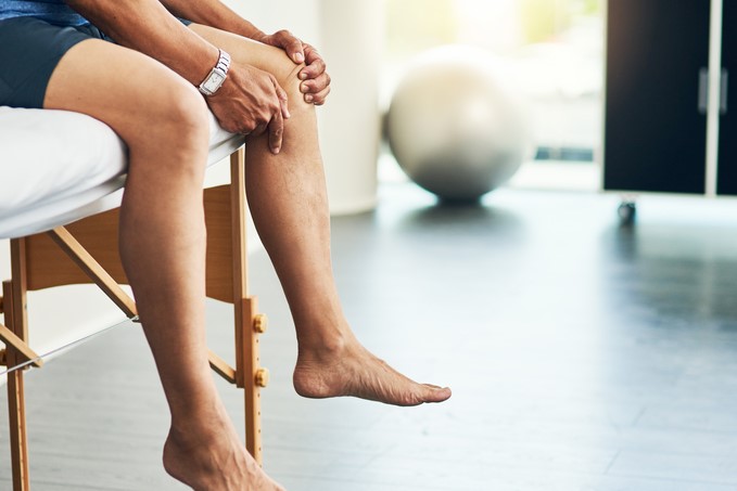 Man rubs his knee while sitting on a physical therapy table.