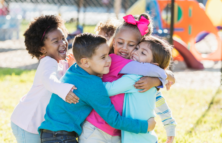 Preschool children do a group hug on a playground.