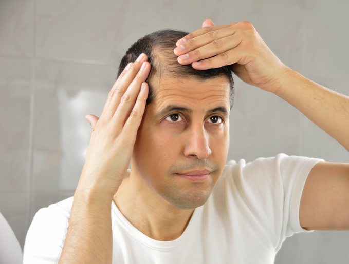 A man looks in the mirror at his thinning hair.