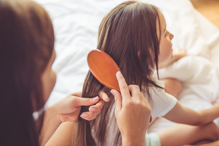 A mother brushes her young daughter's long hair.