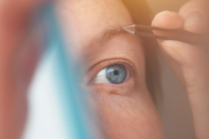 A close-up of a red-headed woman plucking out most of her eyebrow.