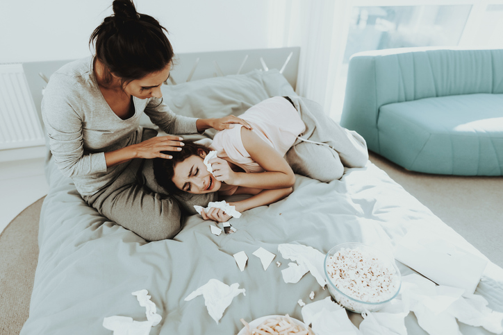 A distraught woman sobs in her friend's lap, surrounded by tissues.