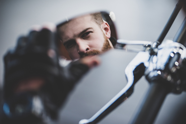 A man checks his reflection in the side mirror of his motorcycle.